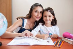 Buena niñera con formación ayudando a niña a hacer los deberes